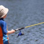 Child holding an affordable beginner fishing pole by a lake