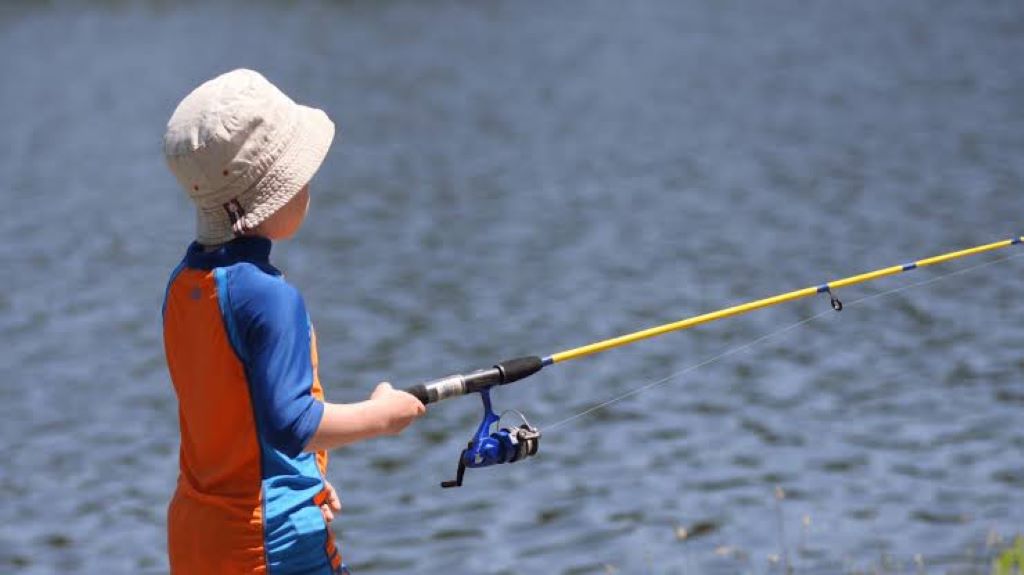 Child holding an affordable beginner fishing pole by a lake