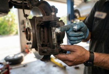 Male mechanic applying ceramic grease to automotive brake components in a bright garage.